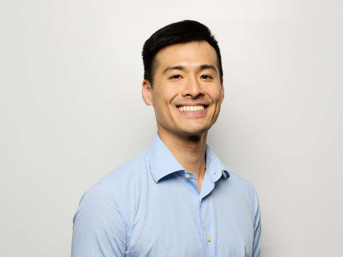 Dr Timothy Wong in a light blue checkered shirt smiling with one hand in his pocket against a plain light background